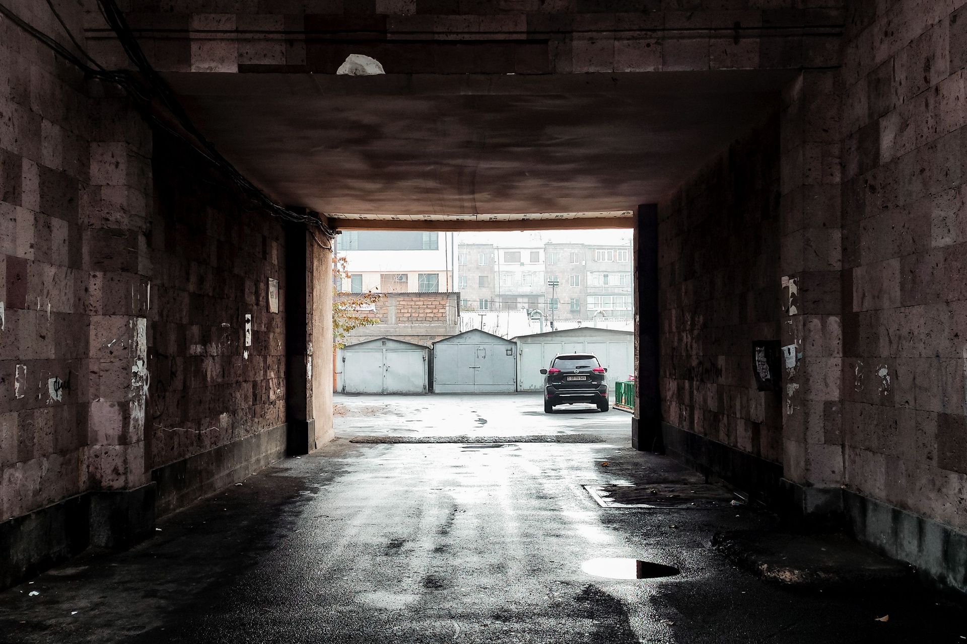 Moody view of a parked SUV through a gritty urban tunnel in Yerevan, Armenia. Reflections on wet asphalt enhance the scene's mood.
